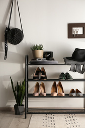 Photo of Black shelving unit with shoes and different accessories near white wall in hall