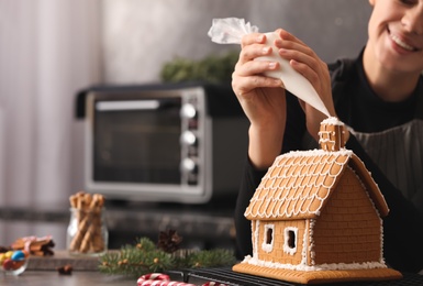 Woman decorating gingerbread house with icing at table, closeup
