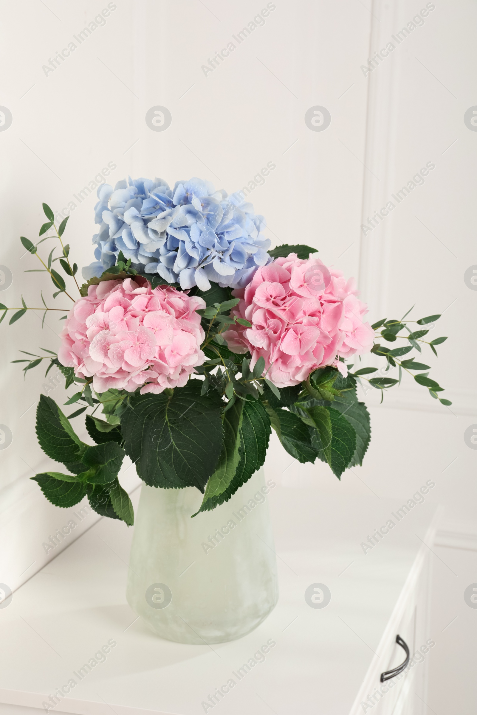 Photo of Beautiful hortensia flowers in vase on table near white wall