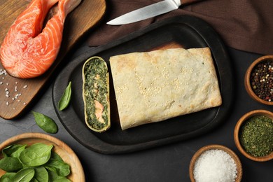 Flat lay composition of delicious strudel with salmon and spinach served on dark table