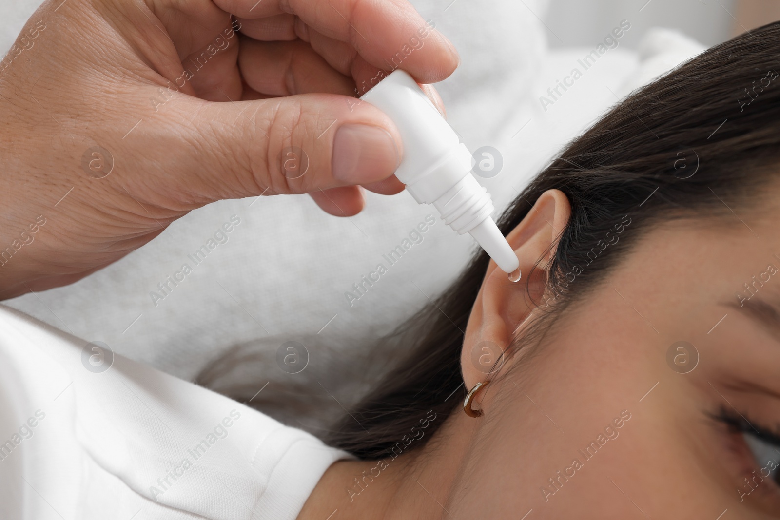 Photo of Senior man dripping medication into woman's ear on sofa, closeup