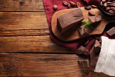 Photo of Pieces of tasty milk chocolate and cocoa beans on wooden table, flat lay. Space for text