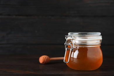 Photo of Jar of organic honey on wooden table against dark background. Space for text