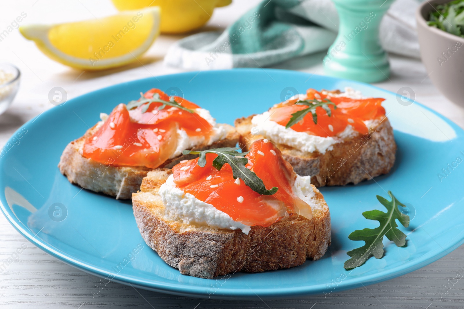 Photo of Delicious sandwiches with cream cheese, salmon and arugula on light blue plate, closeup