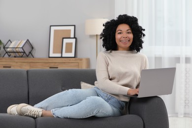 Photo of Happy young woman using laptop on sofa indoors