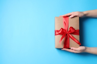 Photo of Woman with gift box on light blue background, top view. Space for text