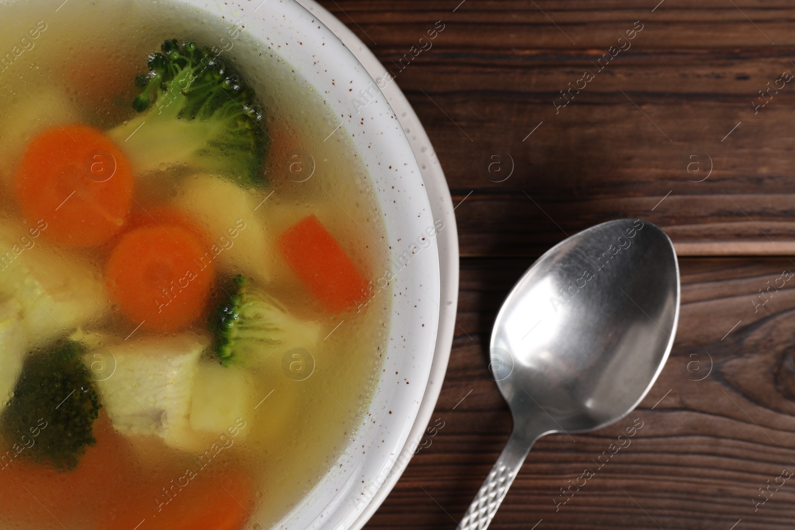Photo of Tasty chicken soup with vegetables in bowl served on wooden table, top view
