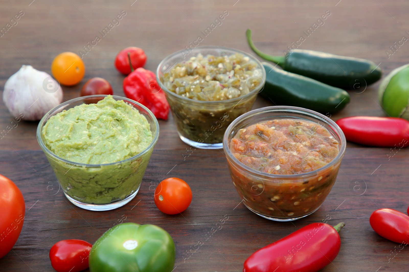 Photo of Tasty salsa sauces and ingredients on wooden table