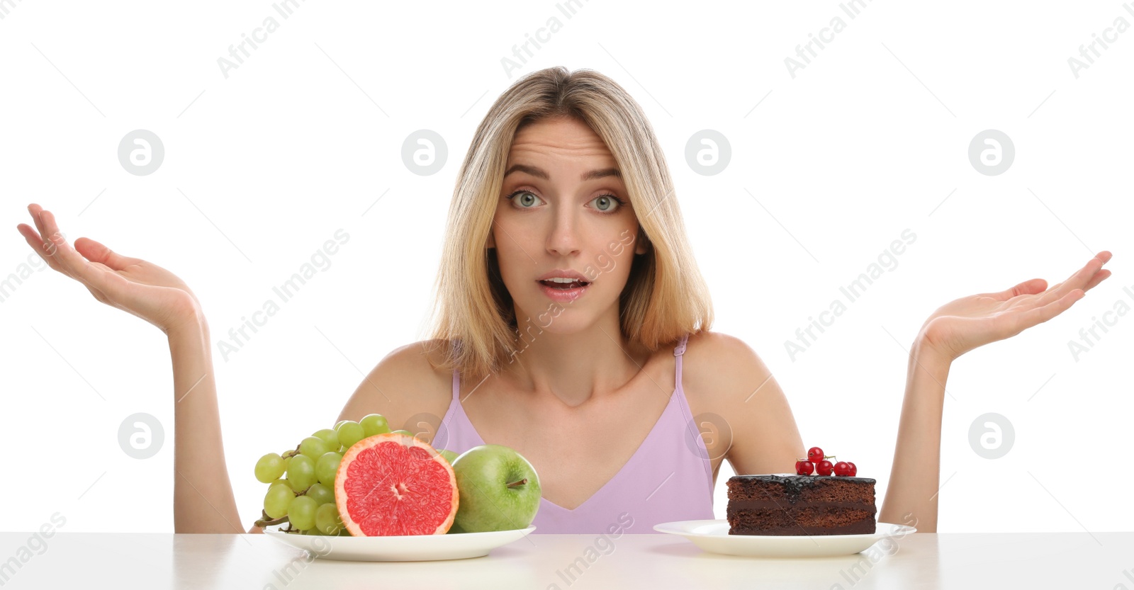 Photo of Woman choosing between cake and healthy fruits at table on white background