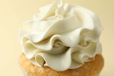 Tasty vanilla cupcake with cream on pale yellow background, closeup