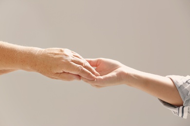 Photo of Helping hands on gray background, closeup. Elderly care concept