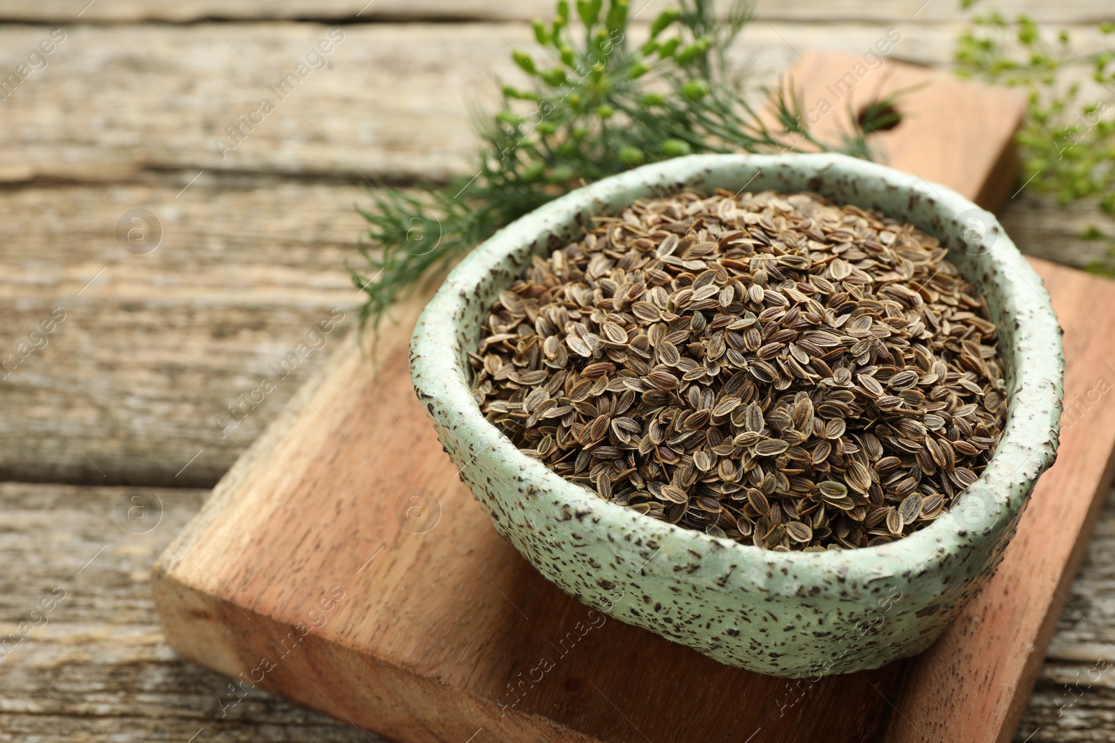 Photo of Board with bowl of dry seeds and fresh dill on wooden table, closeup. Space for text