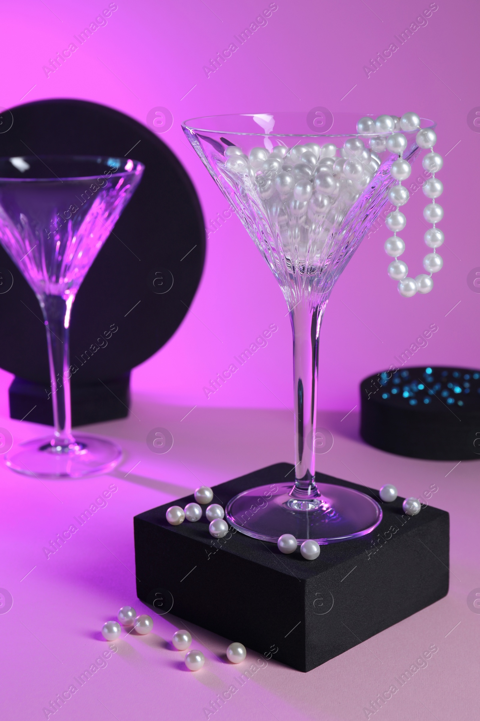 Photo of Beautiful composition with martini glasses and pearls on pink background