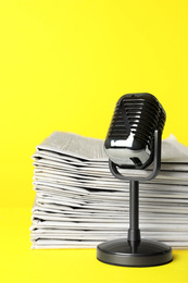 Photo of Newspapers and vintage microphone on yellow background. Journalist's work