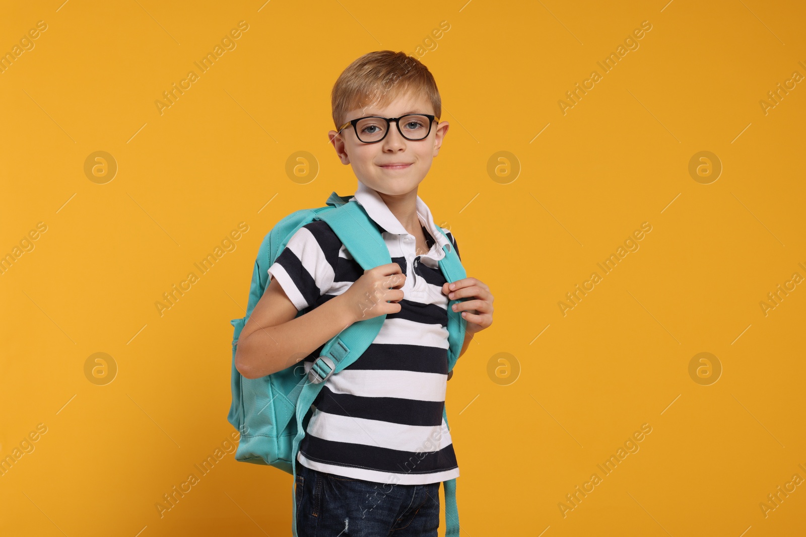 Photo of Happy schoolboy in glasses with backpack on orange background