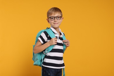 Happy schoolboy in glasses with backpack on orange background