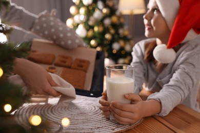 Mother showing her daughter baked Christmas pastry at wooden table, focus on glass of milk