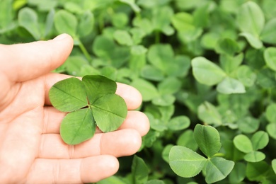 Woman holding four-leaf clover outdoors, closeup