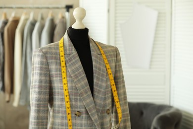 Photo of Mannequin with jacket and measuring tape in tailor shop, space for text