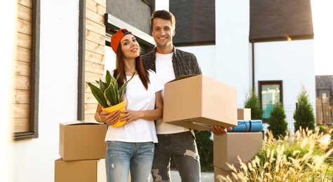 Photo of Happy couple with moving boxes and household stuff near their new house on sunny day