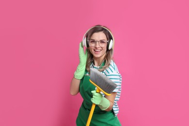 Photo of Beautiful young woman with headphones and floor brush singing on pink background