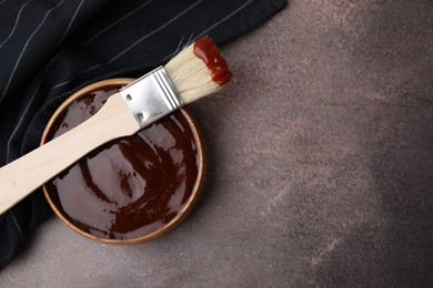 Photo of Marinade in bowl and basting brush on brown table, top view. Space for text