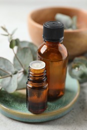 Photo of Bottles of eucalyptus essential oil and plant branches on light grey table