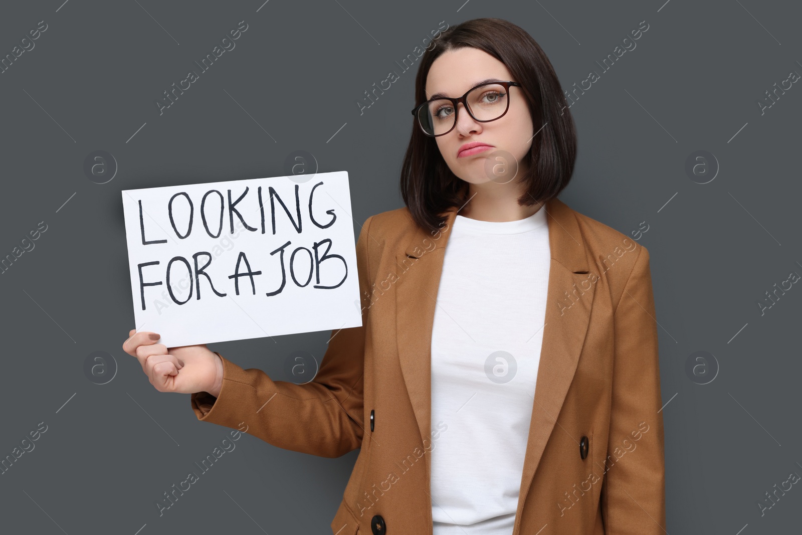 Photo of Upset young unemployed woman holding sign with phrase Looking For A Job on grey background