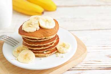 Photo of Plate of banana pancakes served on white wooden table, closeup. Space for text