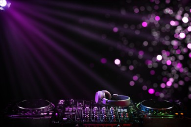 Modern DJ controller and headphones under beams of light in night club, bokeh effect