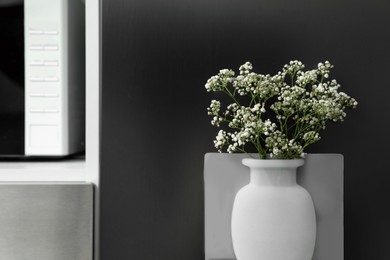Photo of Silicone vase with beautiful gypsophila flowers on fridge in kitchen, space for text