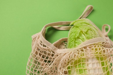 Photo of Fresh ripe Chinese cabbage in net bag on light green background, closeup. Space for text