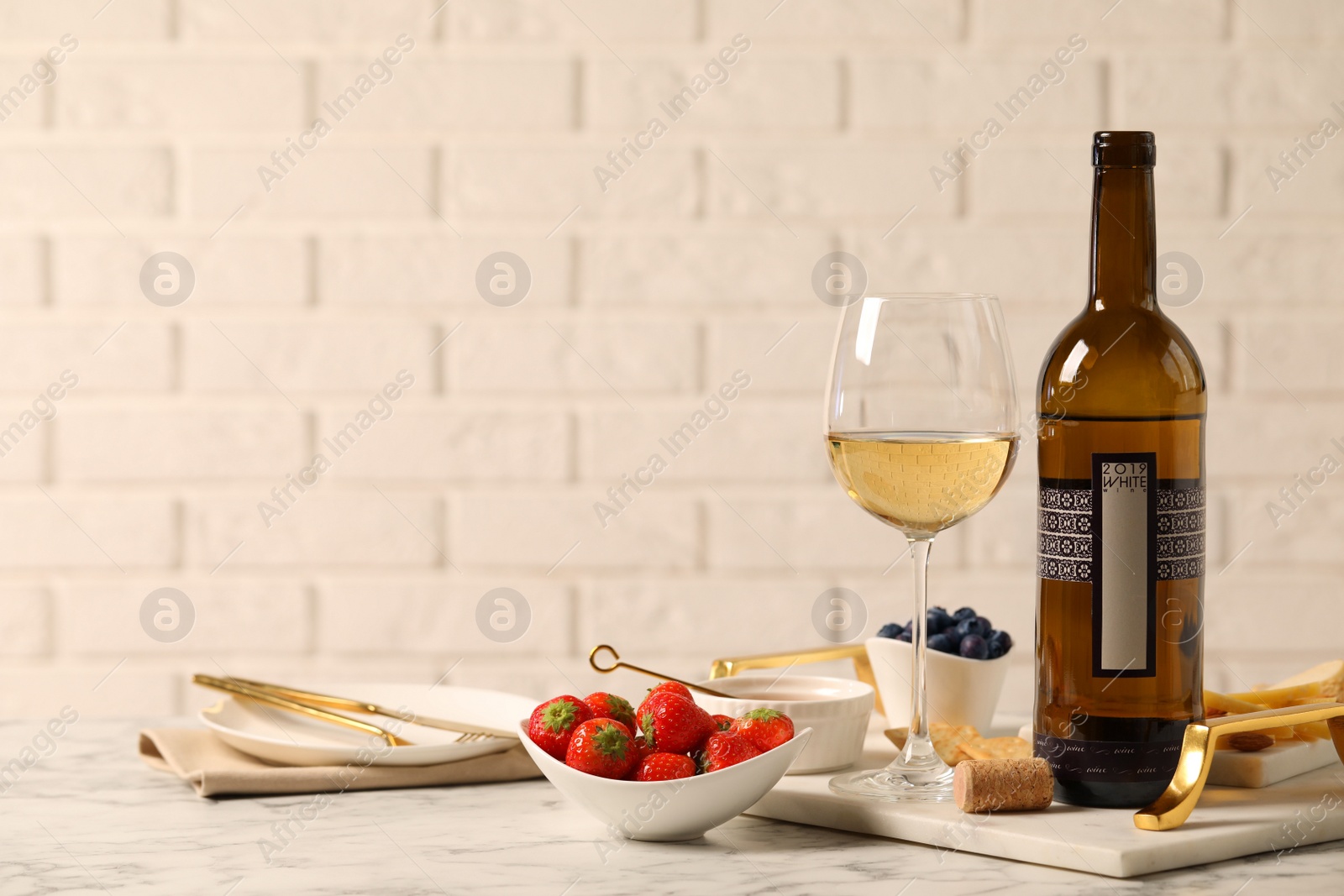 Photo of Bottle of wine, glass and delicious snacks on white marble table