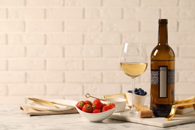 Bottle of wine, glass and delicious snacks on white marble table