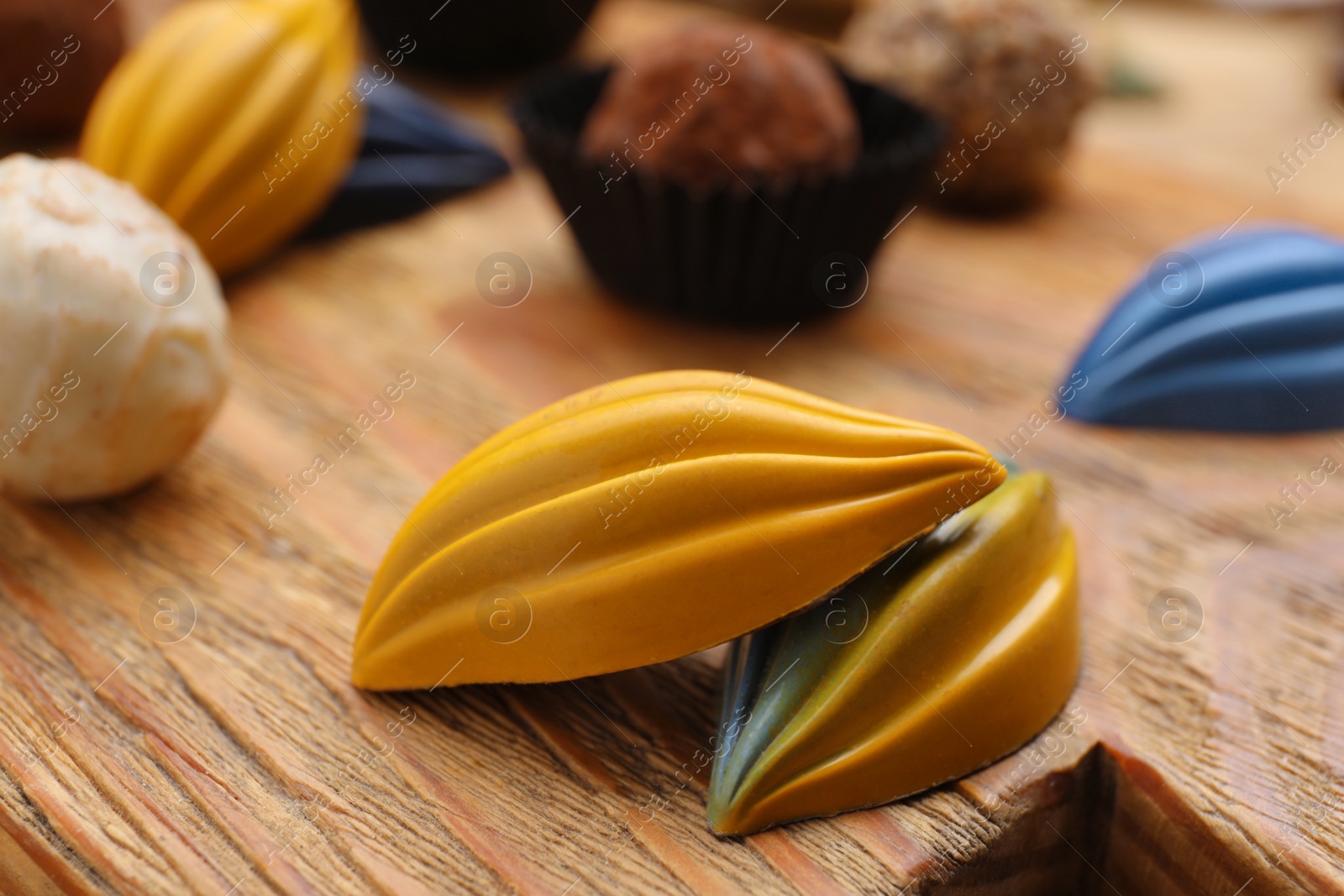 Photo of Different tasty chocolate candies on wooden board, closeup