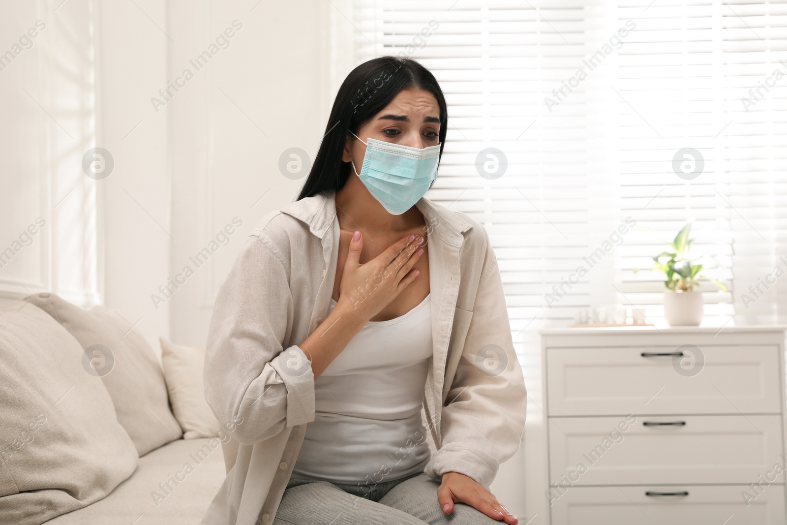 Photo of Young woman with protective mask suffering from breathing problem on sofa at home