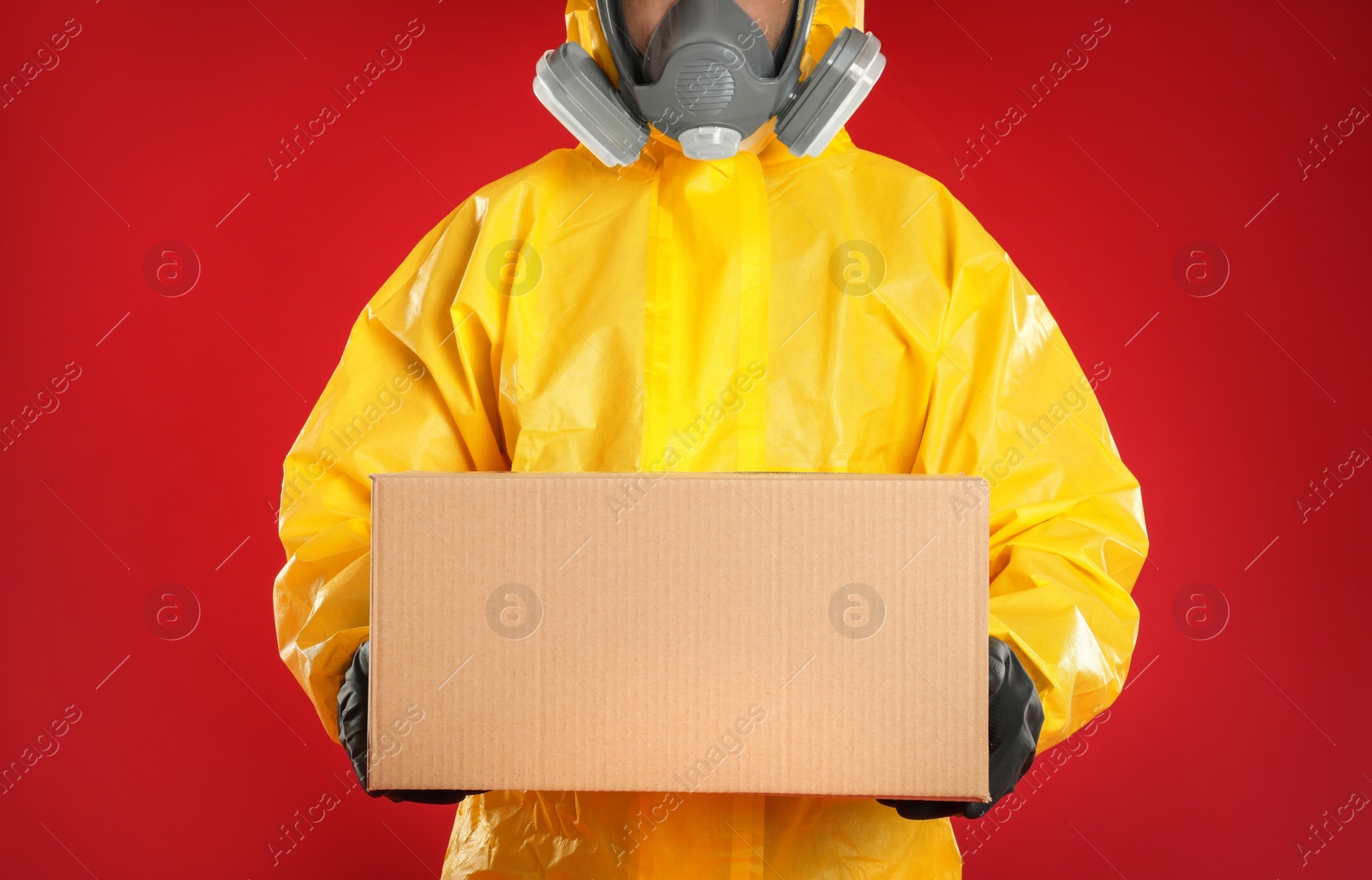 Photo of Man wearing chemical protective suit with cardboard box on red background, closeup. Prevention of virus spread