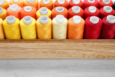 Photo of Container with set of color sewing threads on wooden background