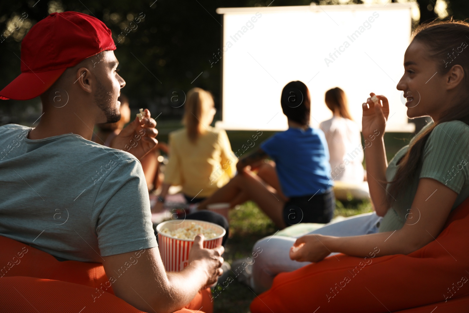 Photo of Young couple with popcorn watching movie in open air cinema. Space for text