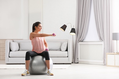 Photo of Young woman doing exercise with dumbbells on fitness ball at home. Space for text