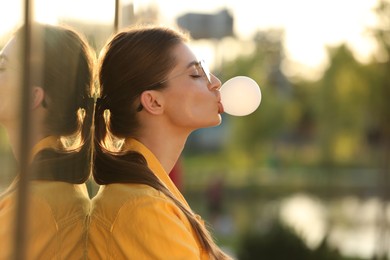 Photo of Beautiful young woman in glasses blowing bubble gum outdoors. Space for text
