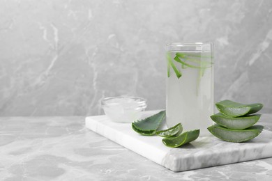 Photo of Tasty aloe juice in glass and cut fresh leaves on light grey marble table, space for text