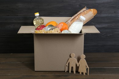 Humanitarian aid for elderly people. Cardboard box with donation food and figures of couple on wooden table, closeup