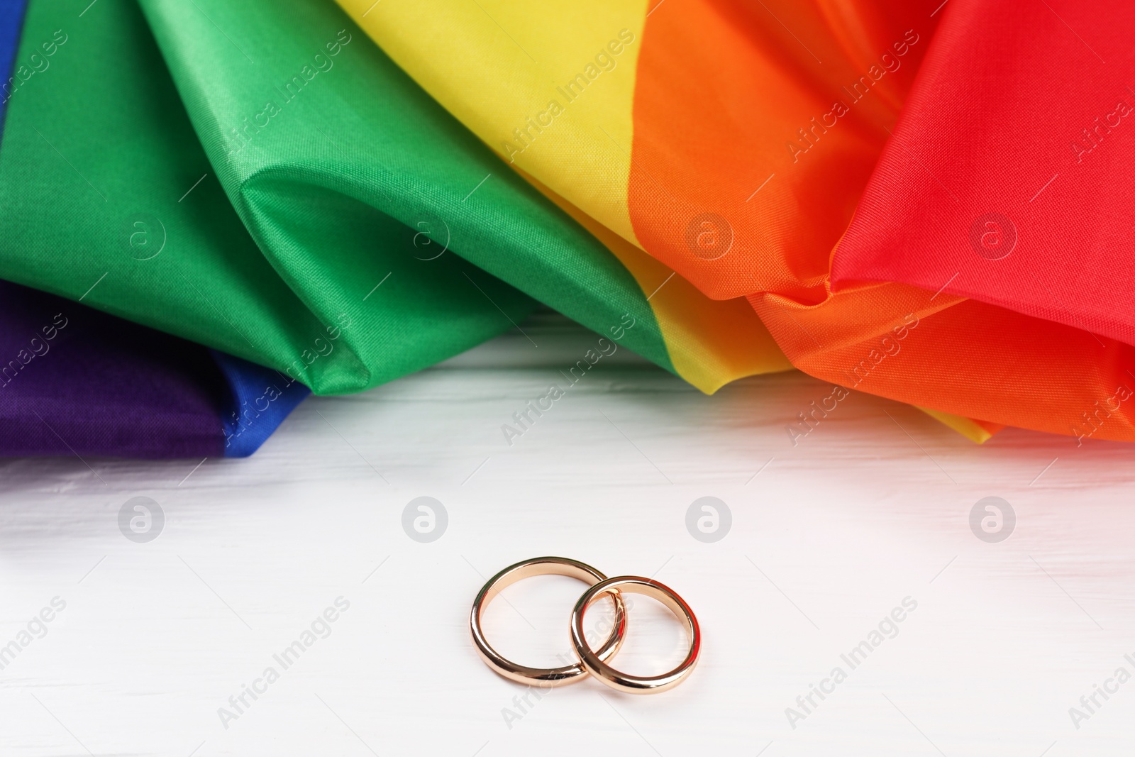 Photo of Rainbow LGBT flag and wedding rings on white wooden table, closeup