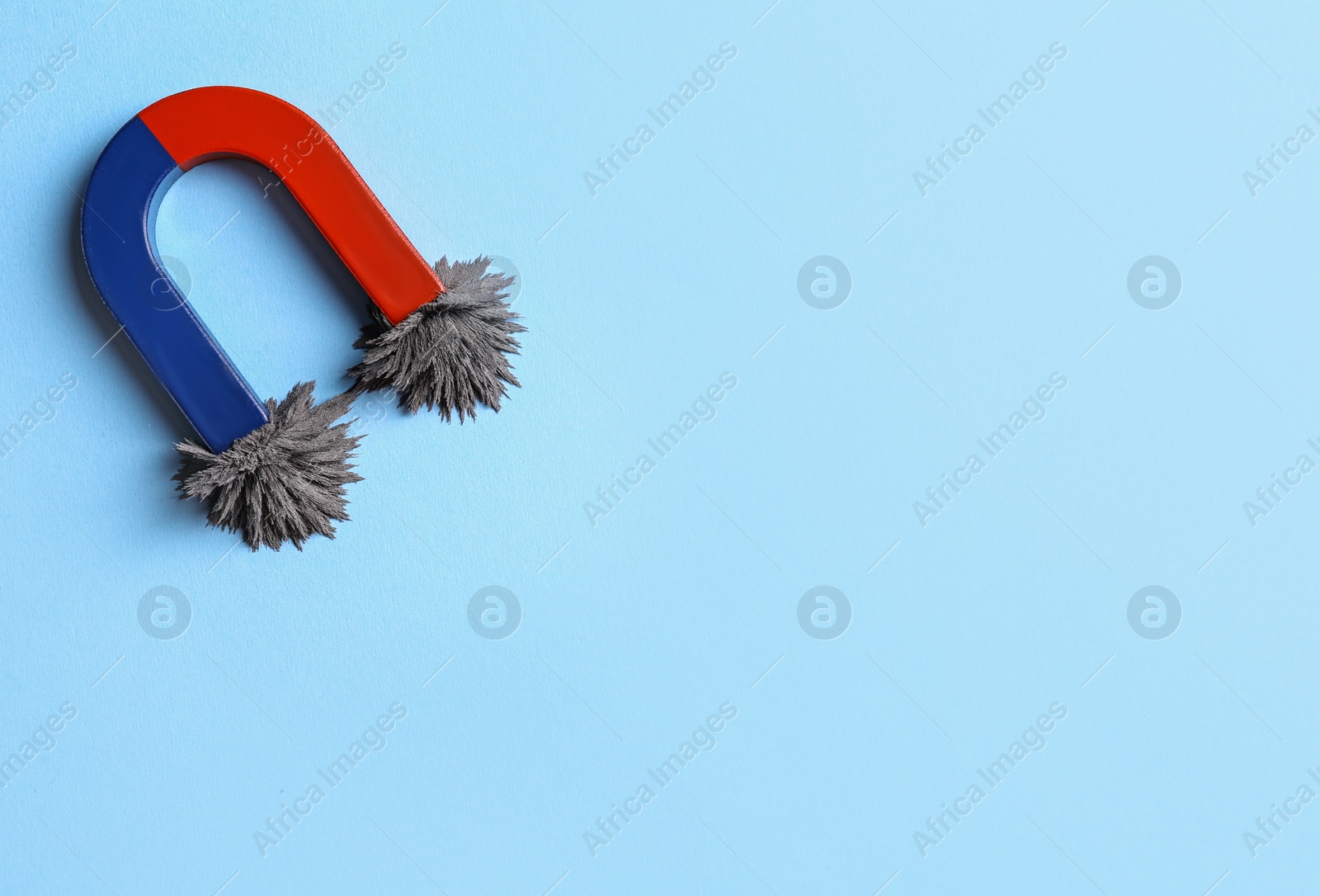 Photo of Horseshoe magnet with iron filings on light blue background, top view. Space for text