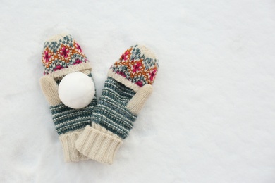 Knitted mittens and snowball on snow outdoors, flat lay. Space for text