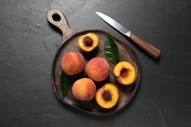 Photo of Delicious juicy peaches, leaves and knife on black textured table, top view