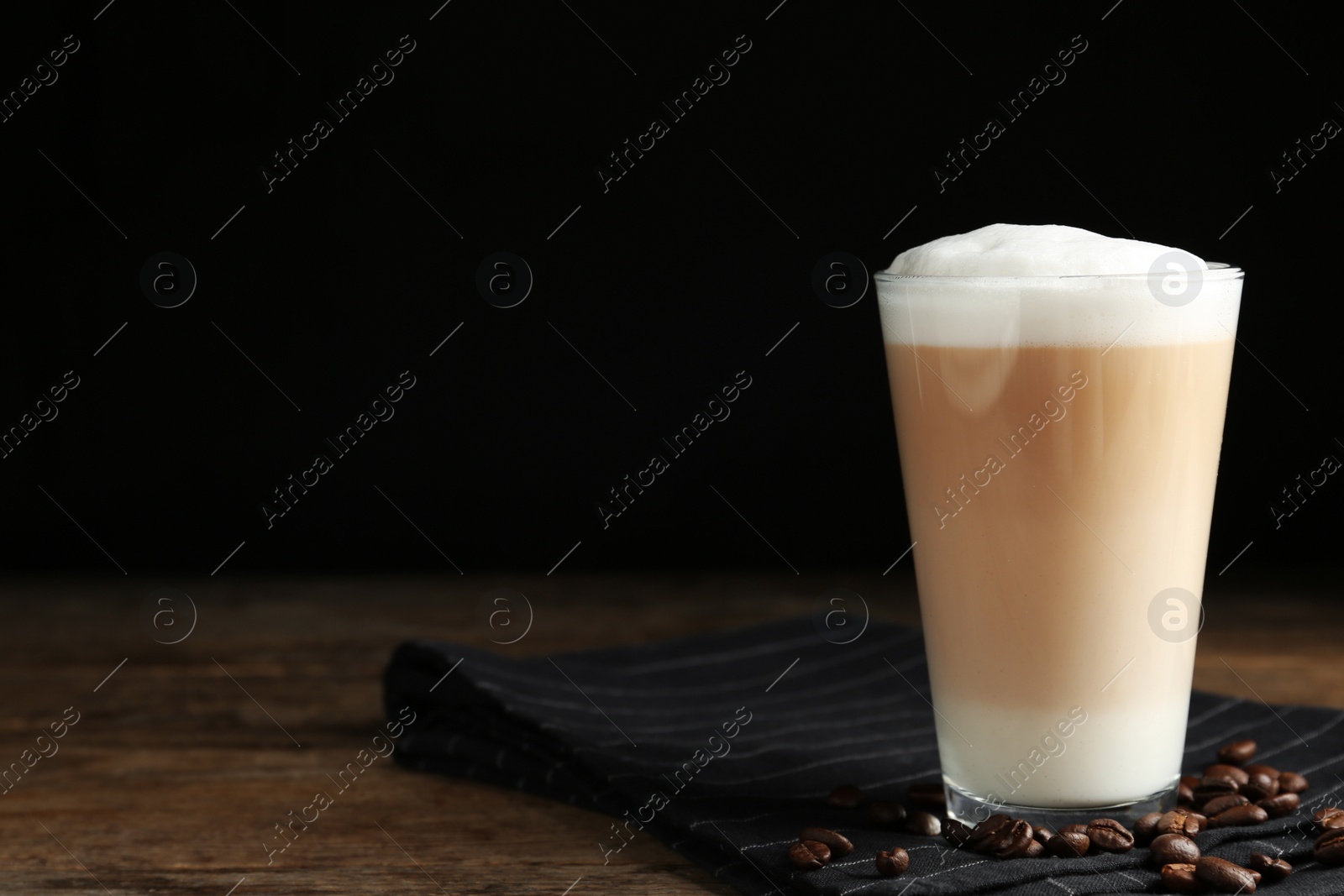 Photo of Delicious latte macchiato and coffee beans on wooden table against black background