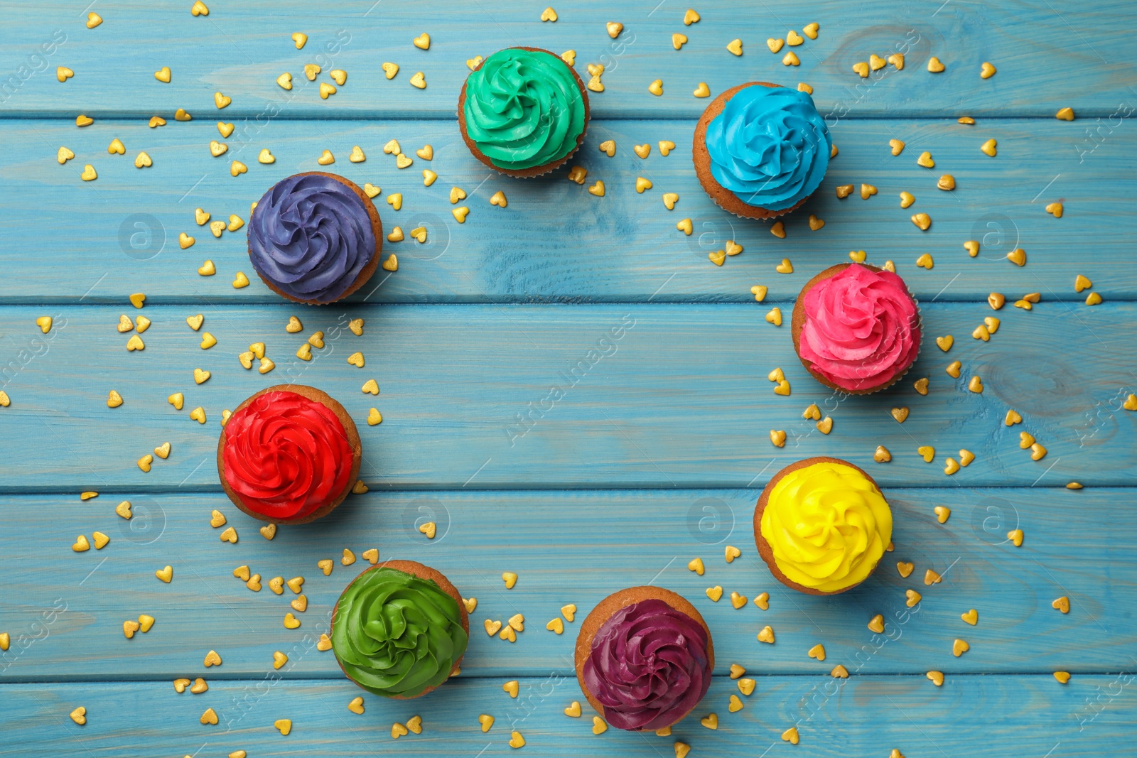 Photo of Frame of delicious colorful cupcakes and heart shaped sprinkles on light blue wooden table, flat lay. Space for text