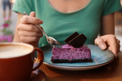 Photo of Woman eating slice of berry cheesecake at table, closeup